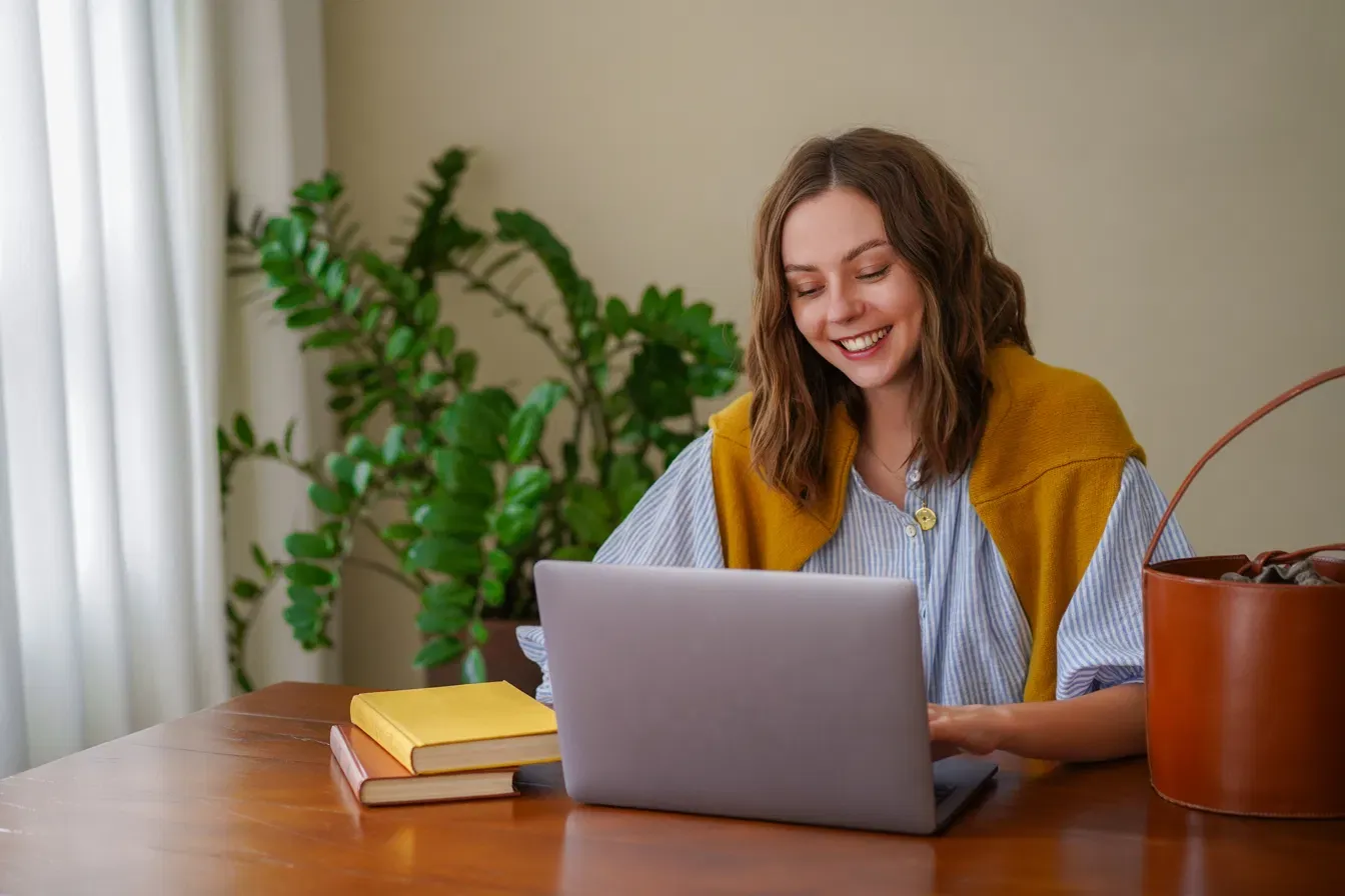 Mulher sorrindo enquanto estuda no notebook em casa